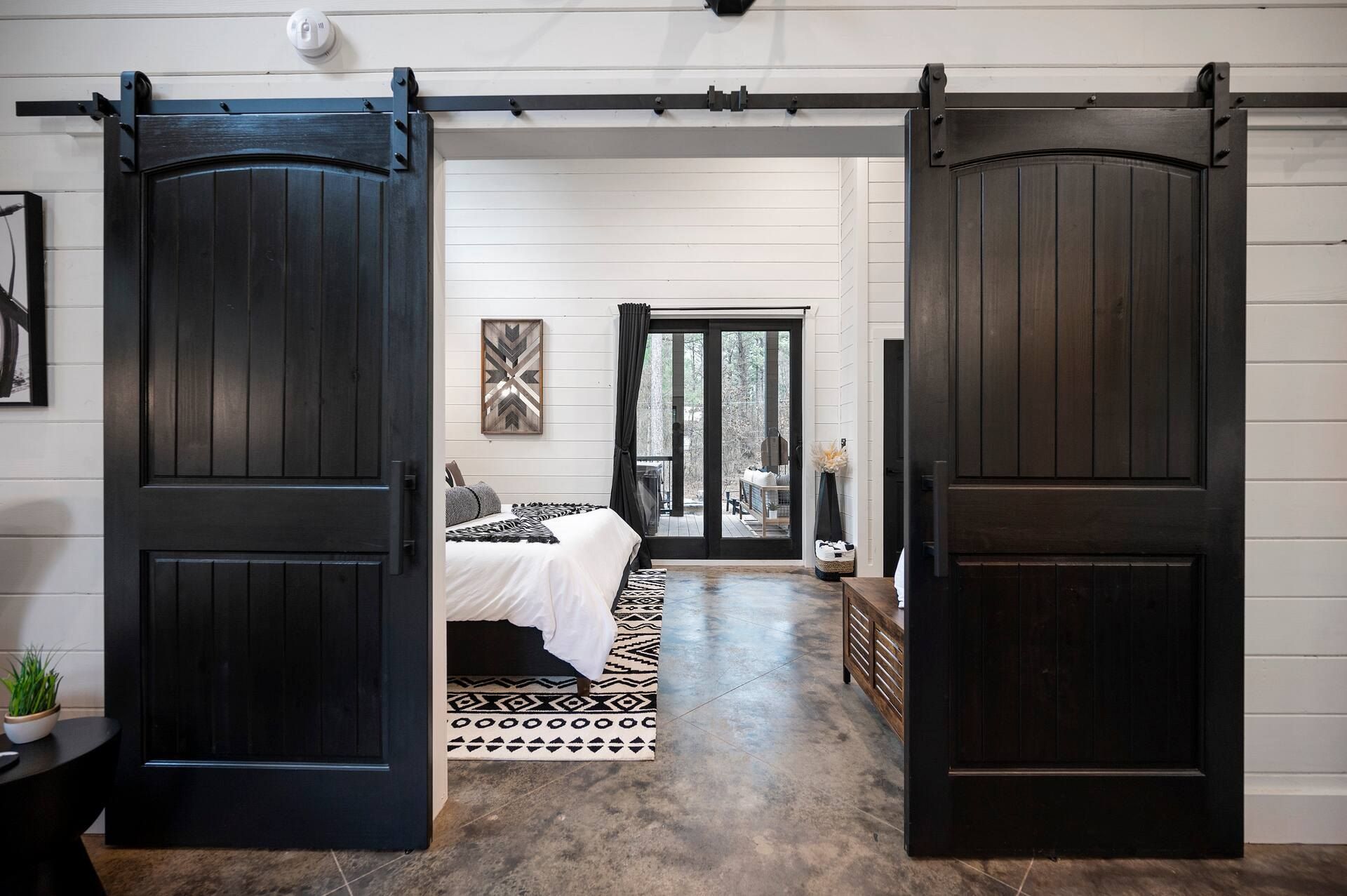 Black barn doors open onto the bedroom, king bed and glass doors to the deck beyond