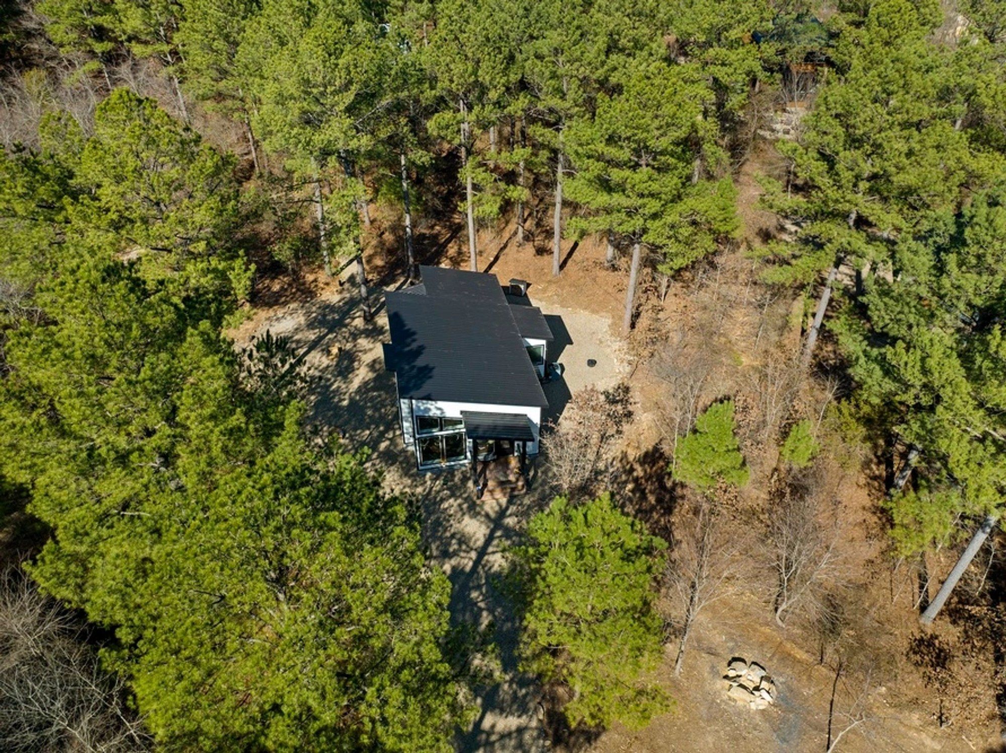 Aerial view of the black cabin alone among tall pine trees