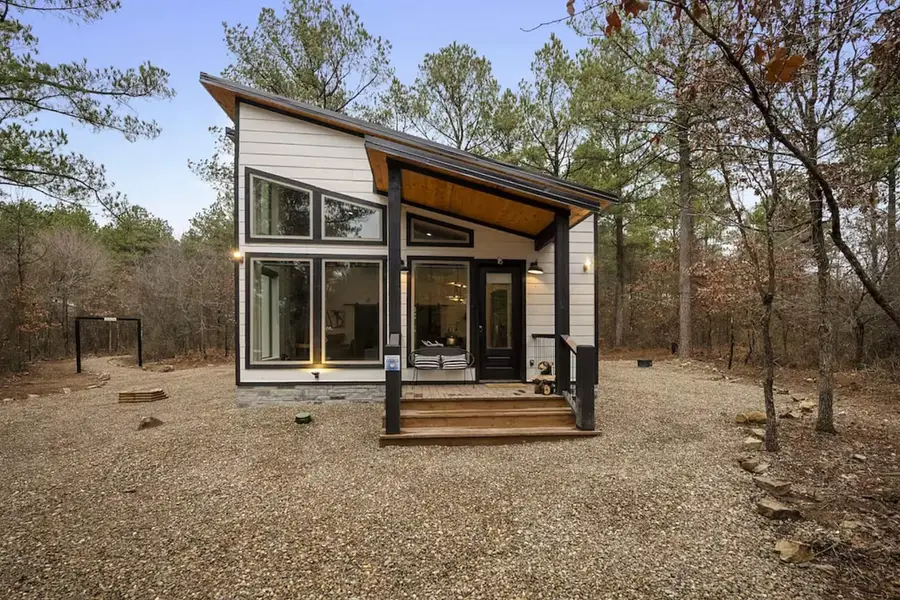 Front of the modern black and white cabin with its covered porch and tall windows among the trees