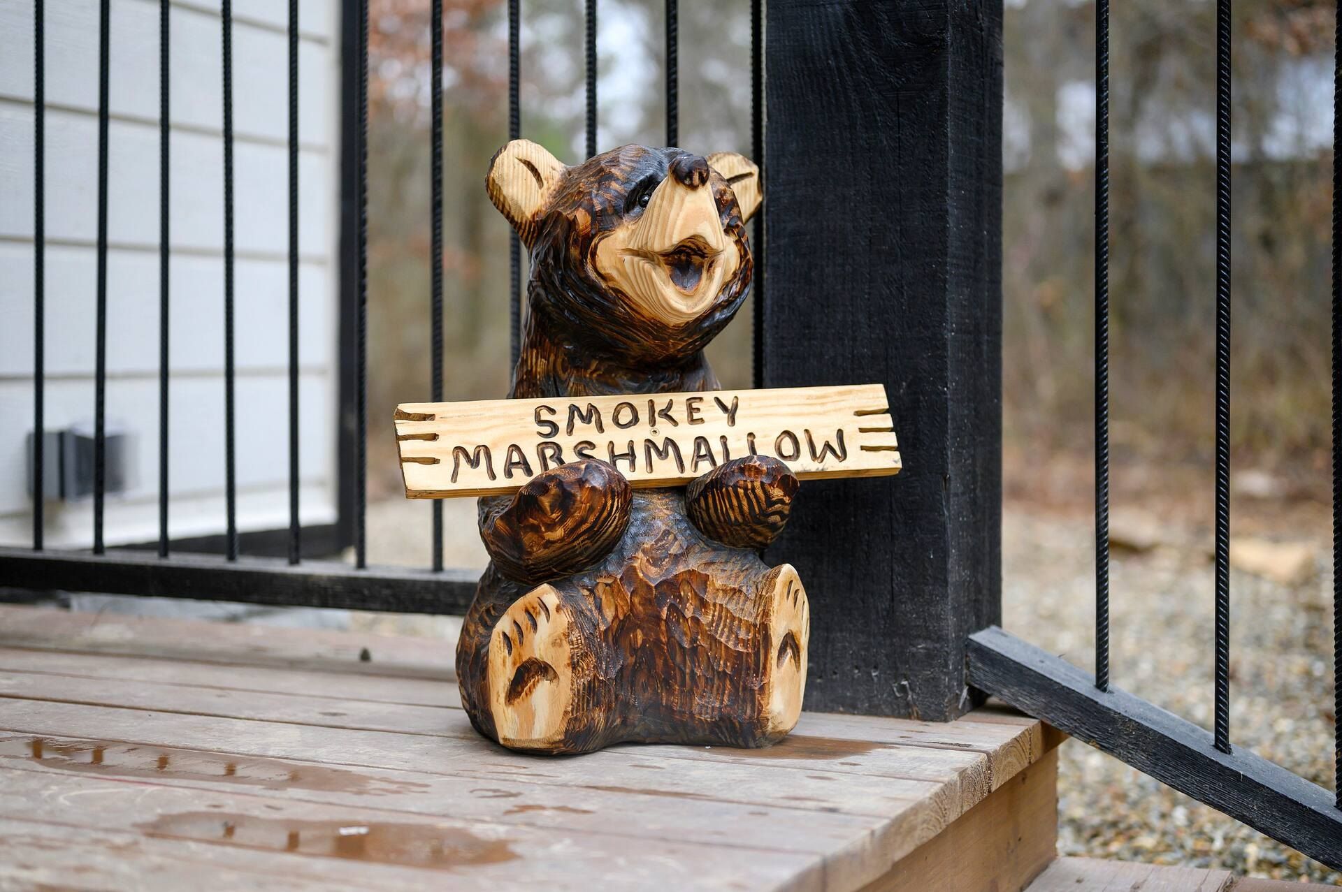 Carved wooden bear holding a Smokey Marshmallow sign on the porch rail