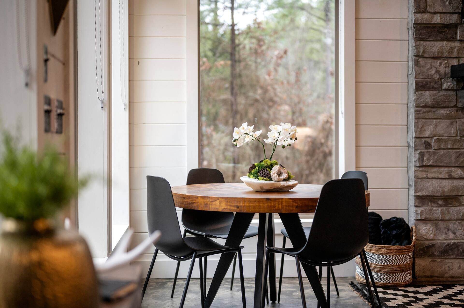 Dining table by the floor-to-ceiling window with an orchid and the stone fireplace beside it