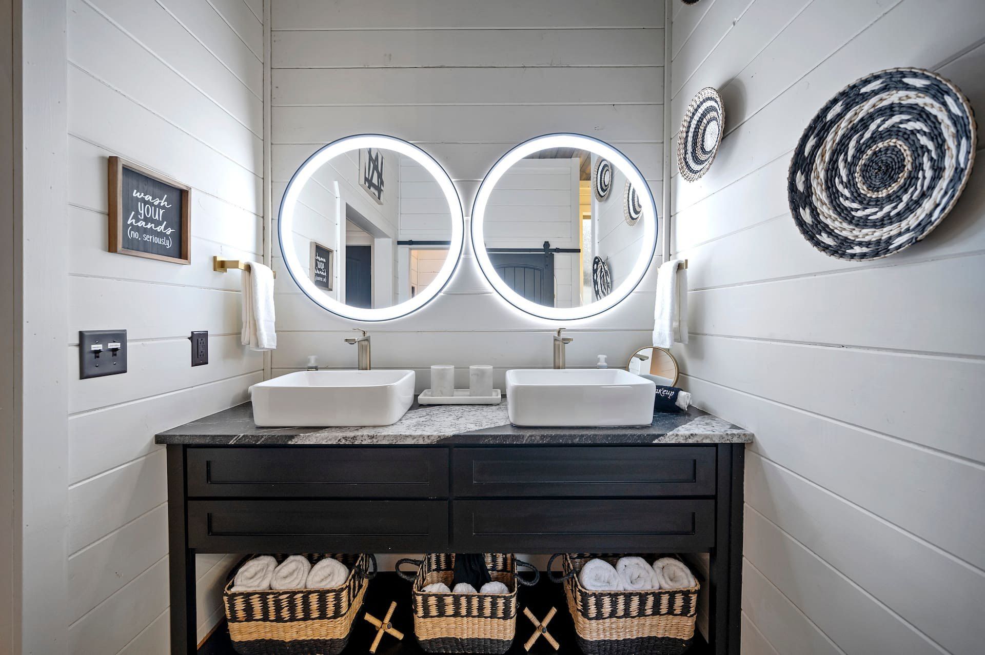 Bathroom double vanity with two lighted round mirrors, vessel sinks and woven wall baskets