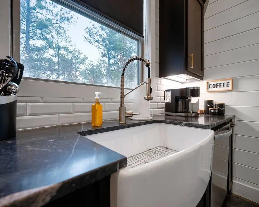 Farmhouse sink below a window into the woods