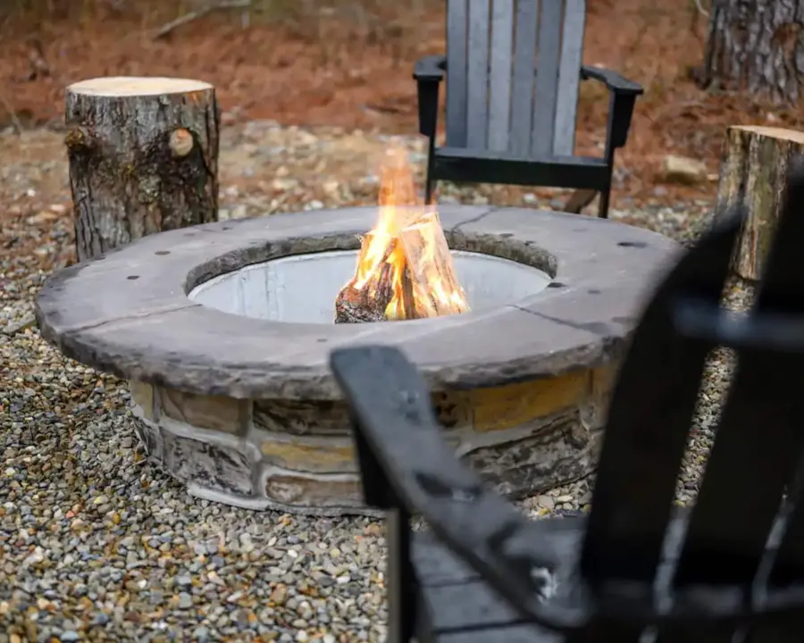 Stone fire pit burning with Adirondack chairs on the gravel