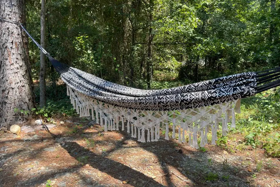 Black and white boho hammock with macrame fringe strung between two pine trees