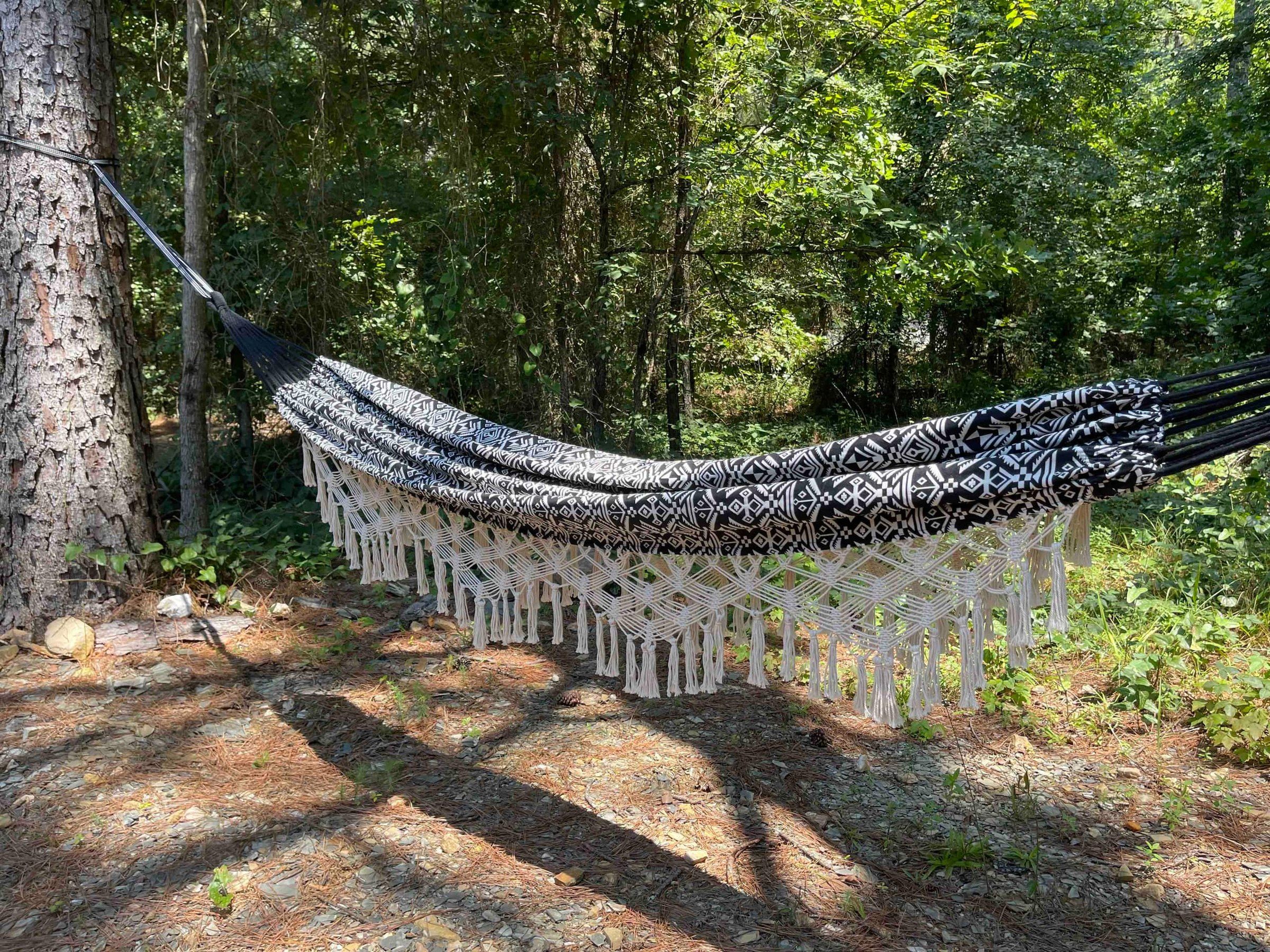Black and white boho hammock with macrame fringe strung between two pine trees