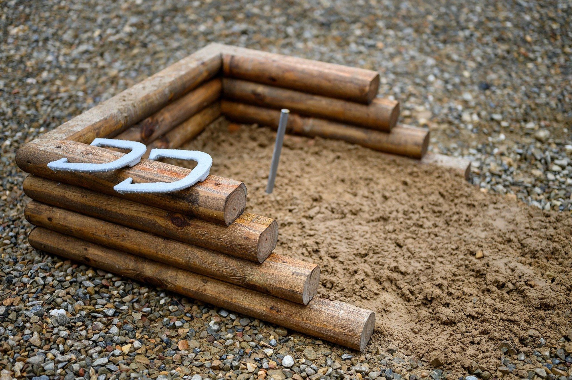 Horseshoe pit framed with logs, two horseshoes on the sand