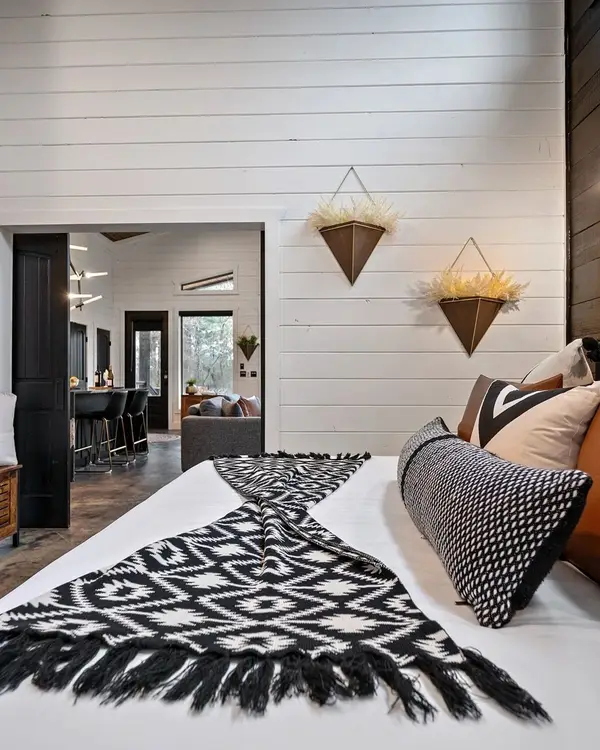 King bedroom with white shiplap walls, leather and woven pillows and a black and white throw