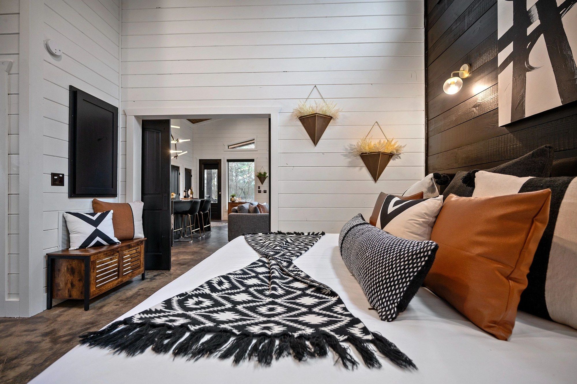 King bedroom with white shiplap walls, leather and woven pillows and a black and white throw