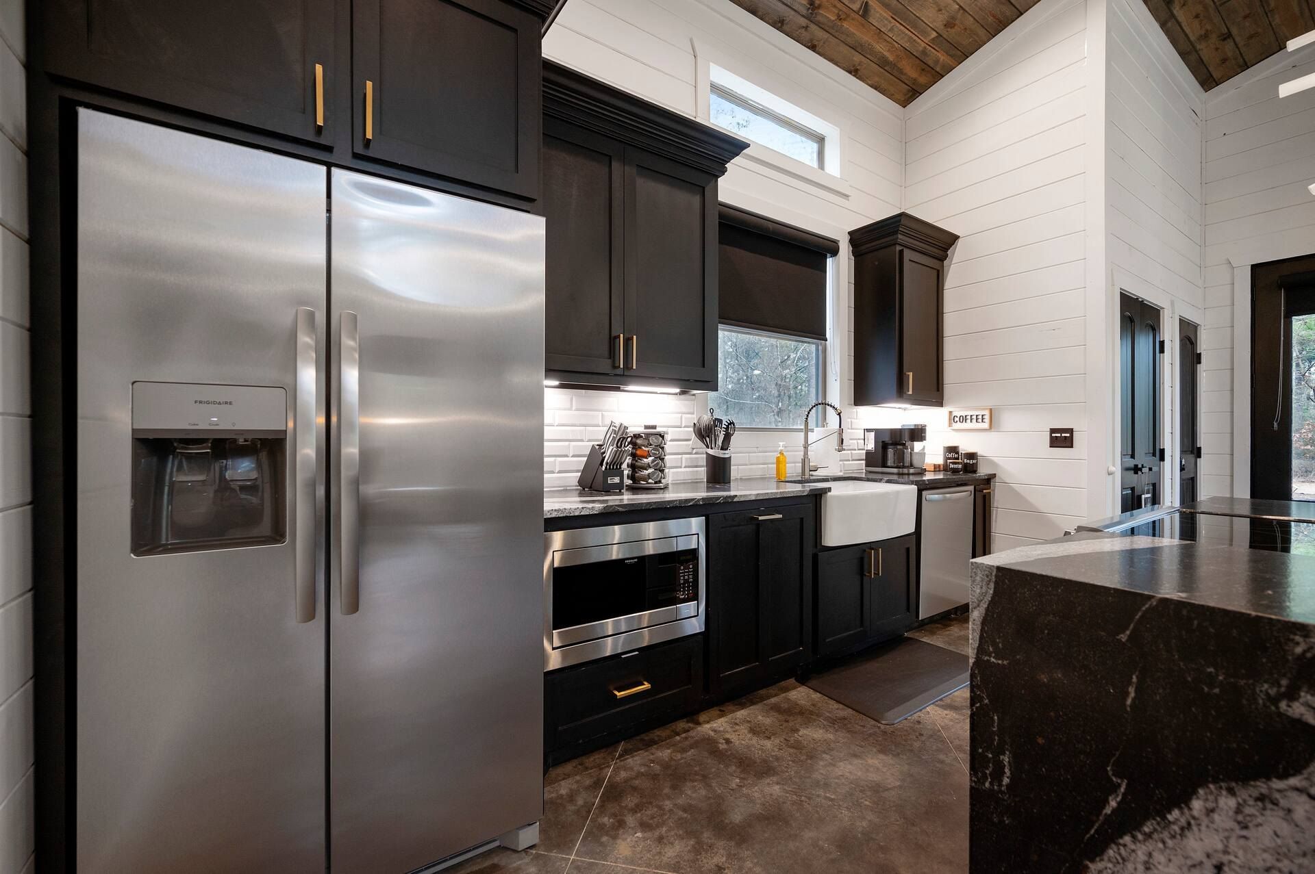 Kitchen with black cabinets, stainless refrigerator and farmhouse sink below the window