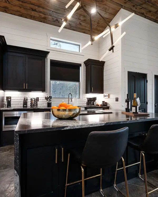 Kitchen with black cabinets, stainless refrigerator and a waterfall-edge granite island with two barstools