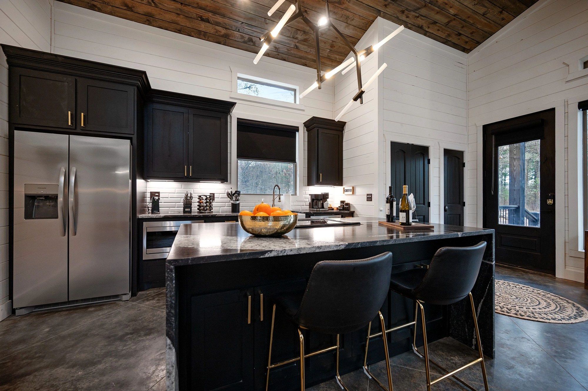 Kitchen with black cabinets, stainless refrigerator and a waterfall-edge granite island with two barstools