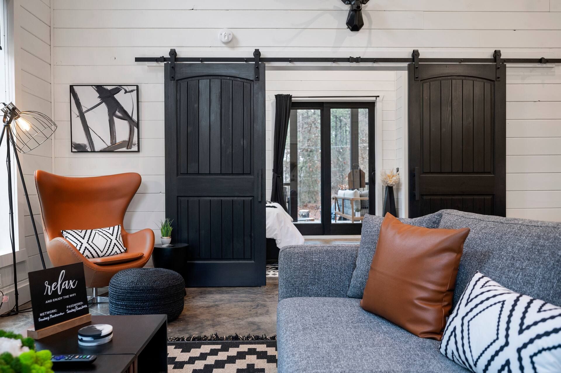 Living room with the black barn doors open to the bedroom, a leather egg chair and the gray sofa