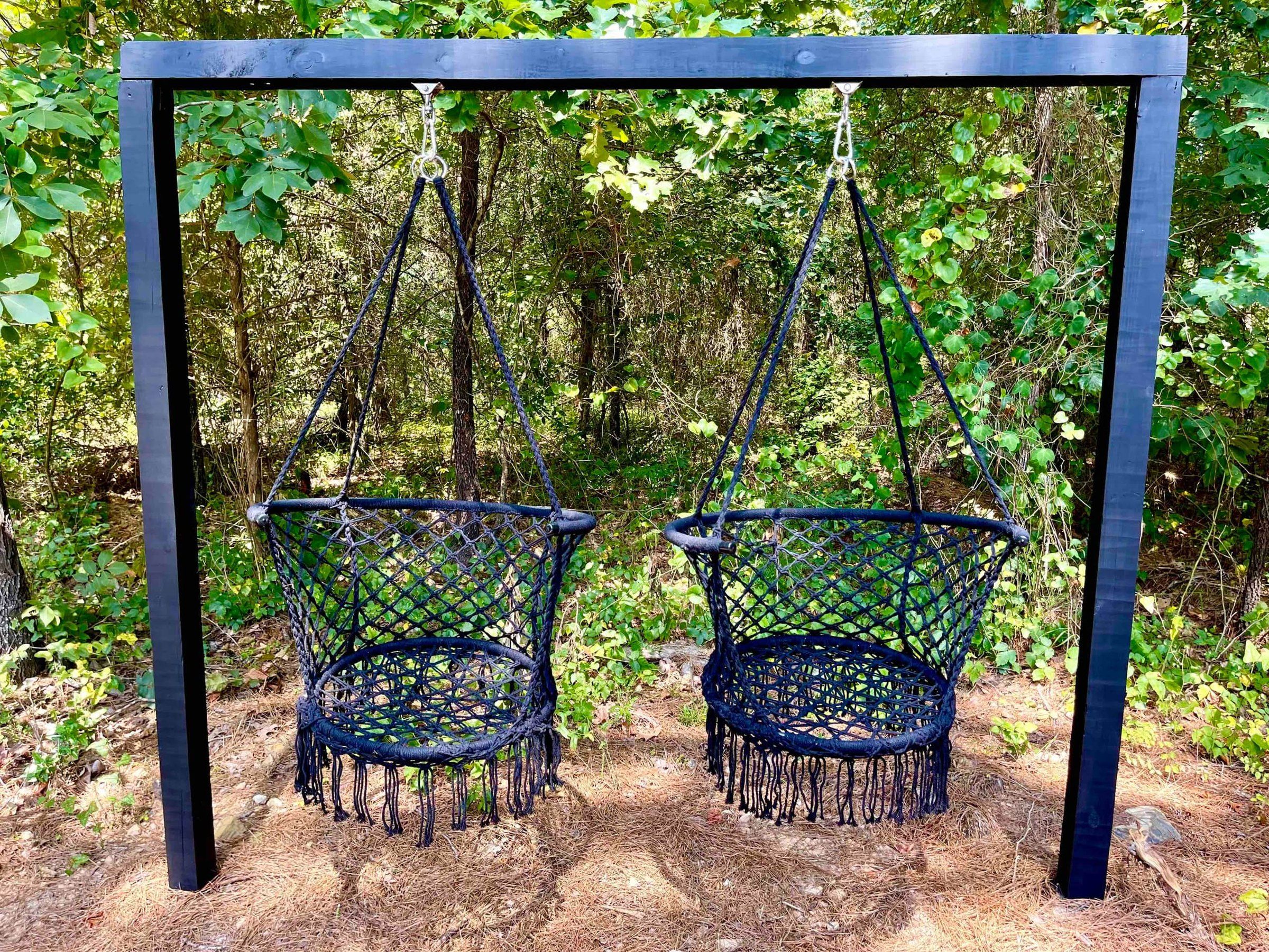 Two hanging macrame swing chairs on a black frame at the edge of the woods
