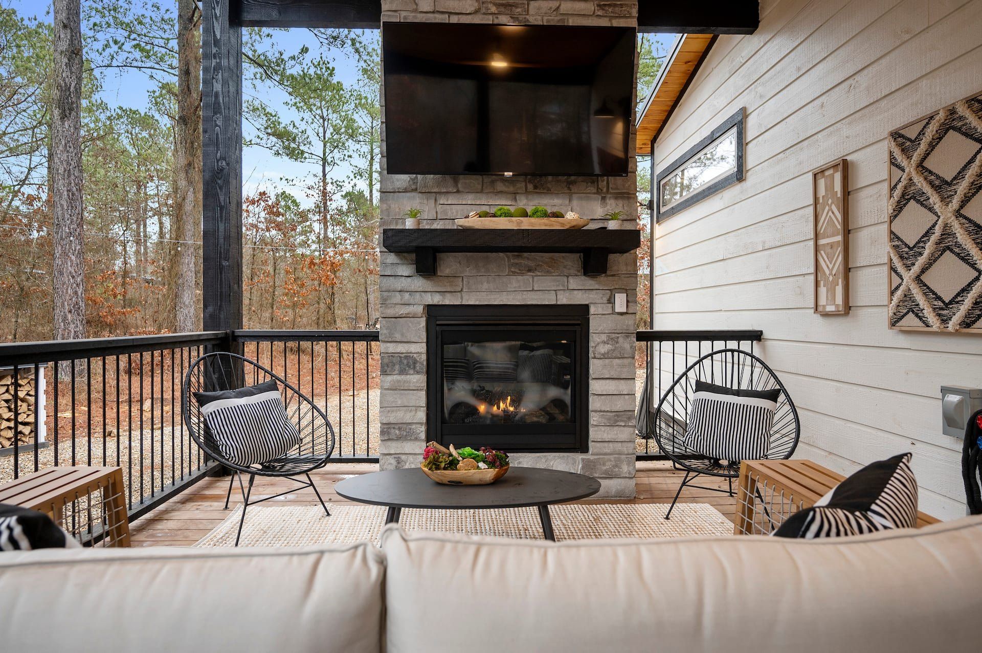 Outdoor stone fireplace on the deck with a TV above it and two wire chairs