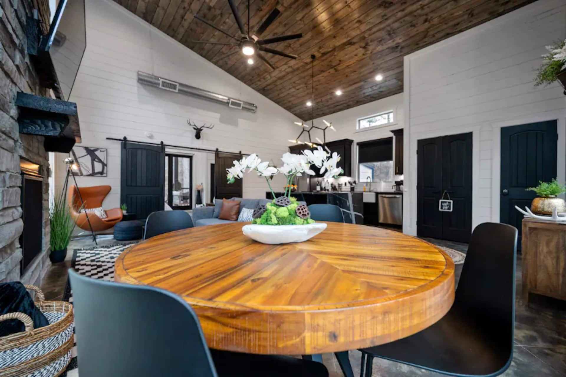 Round wood dining table with four black chairs between the kitchen and the living room