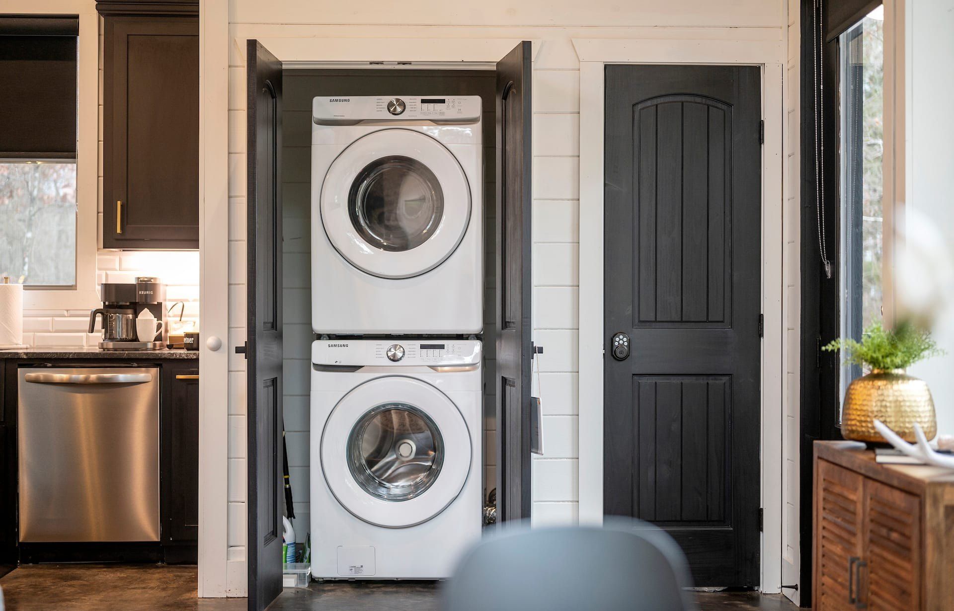 Stacked Samsung washer and dryer in a closet beside the kitchen, dishwasher and coffee maker in view