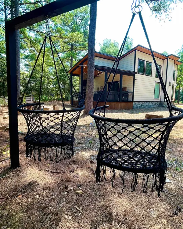 Two black macrame swing chairs on a frame under the pines with the cabin and deck behind